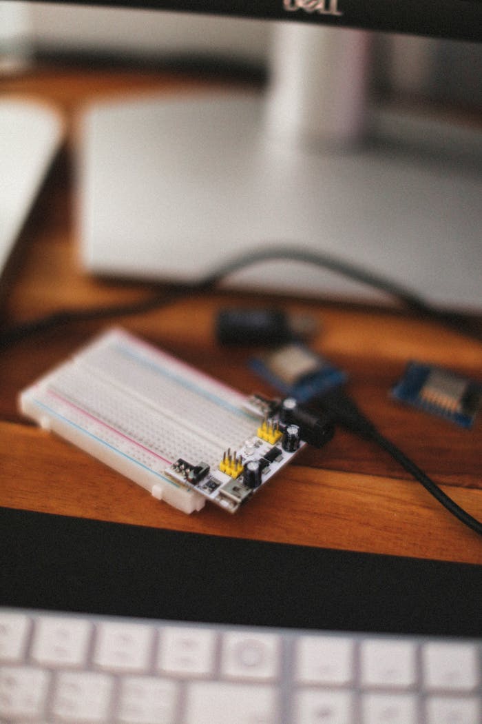 A detailed view of an electronics breadboard and microcontroller on a wooden desk.
